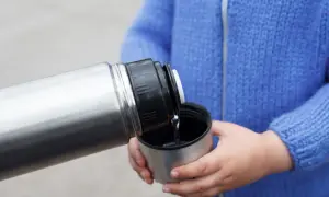 Dziecko nalewa płyn z metalowego termosu do kubka.